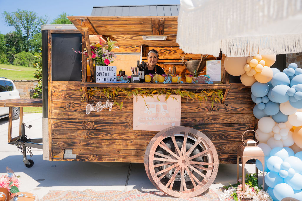 Mobile trailer bar with bartender serving handcrafted cocktails and smiling at guests in Houston