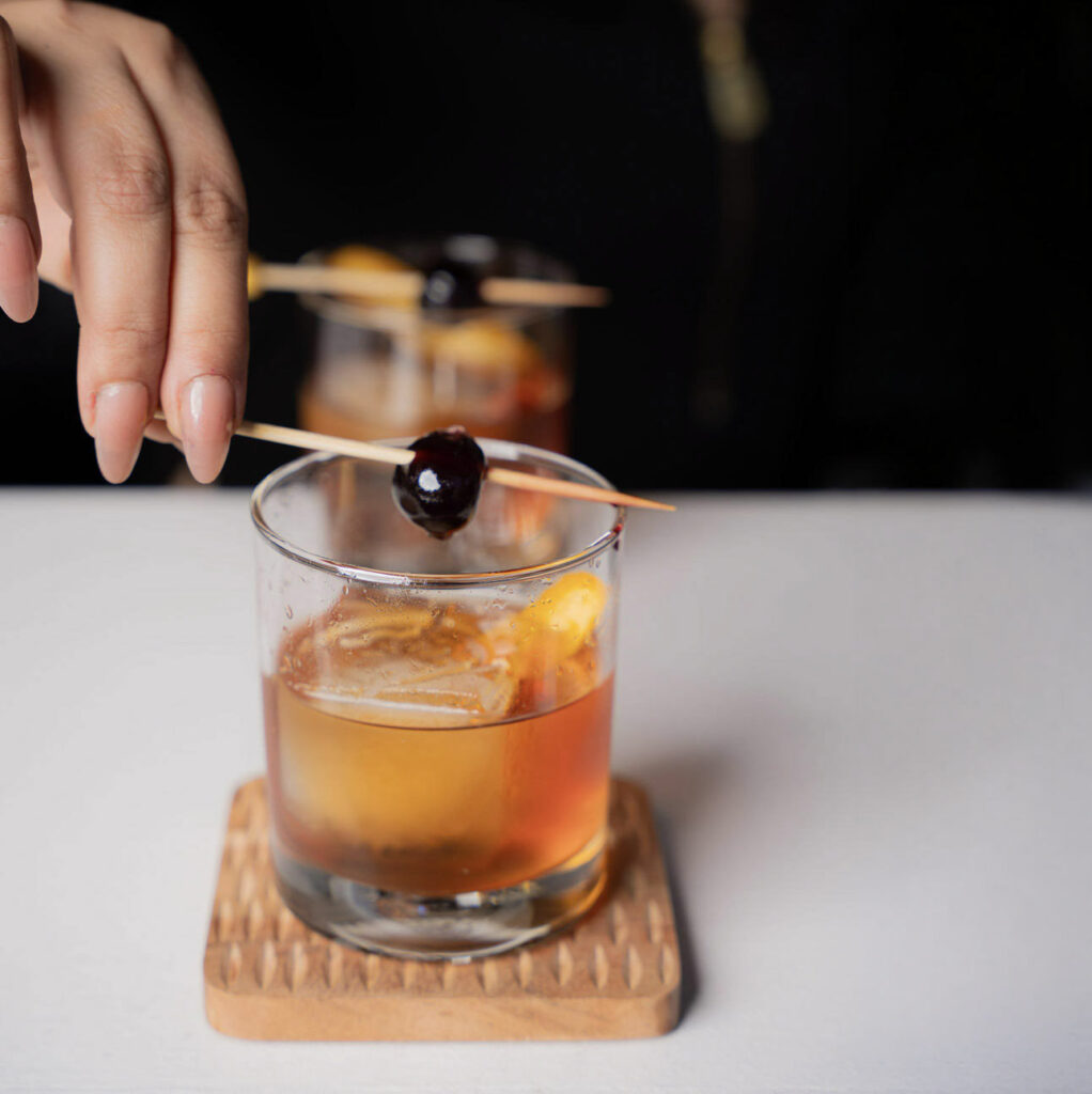 Bartender garnishing a handcrafted Old Fashioned cocktail with a cherry at a Houston event