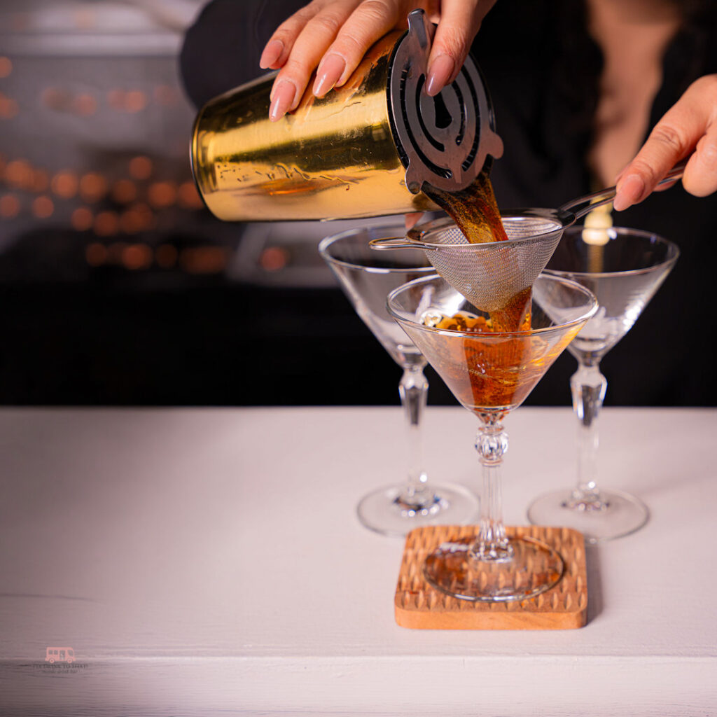 Bartender straining freshly mixed cocktails into martini glasses at a Houston private party