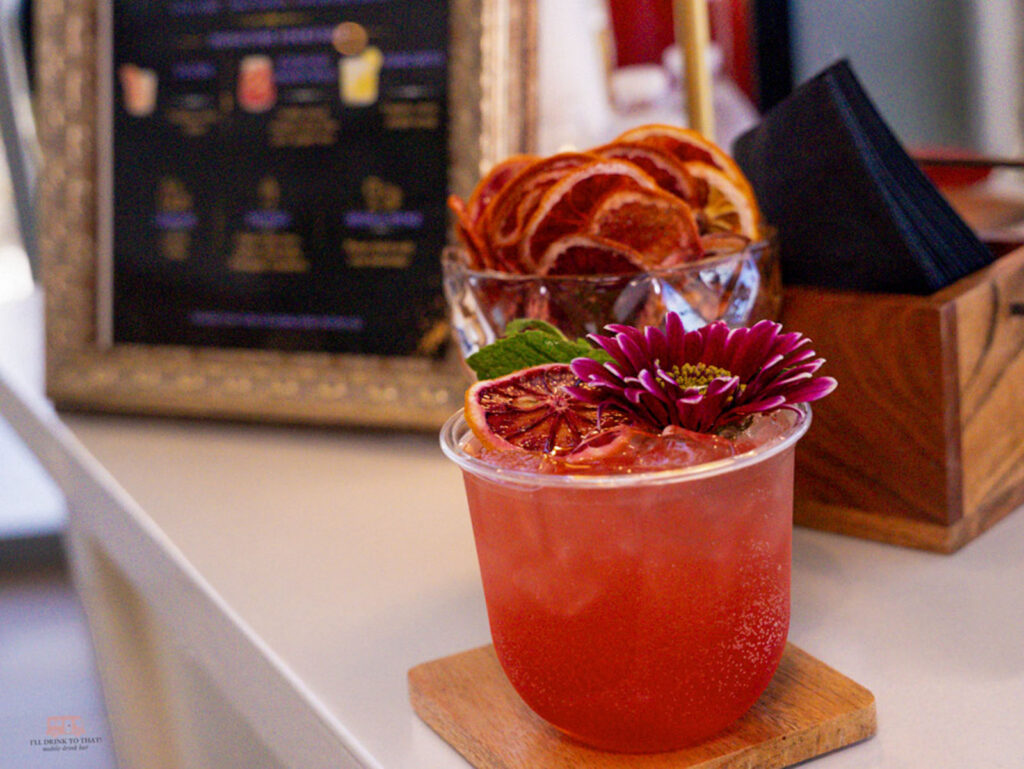 Red handcrafted mocktail garnished with blood orange, mint, and a flower